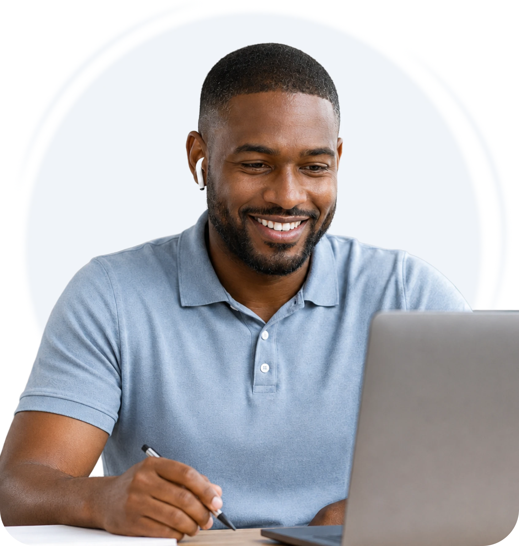 Man smiling while reviewing notes next to his laptop